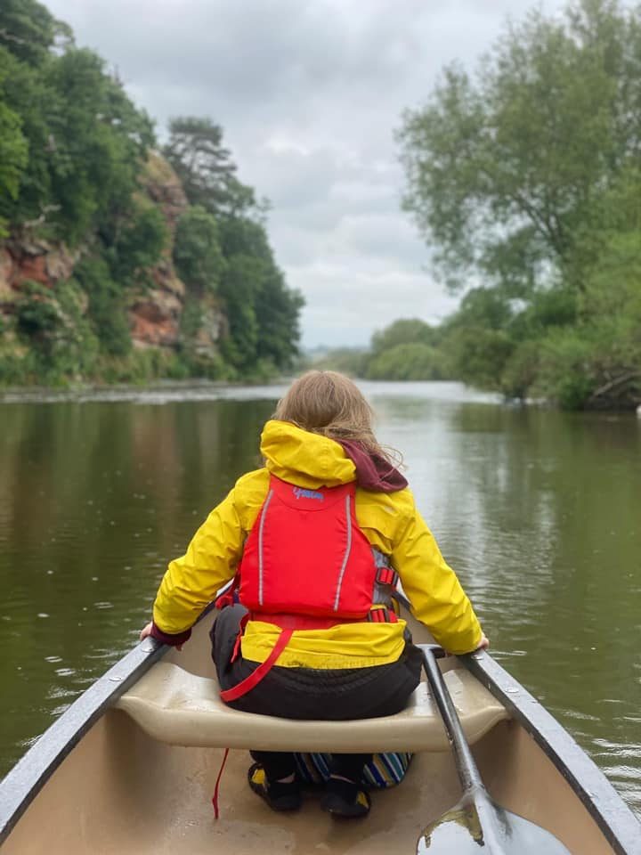 Paddler in a yellow jacket canoeing beneath the red sandstone cliffs